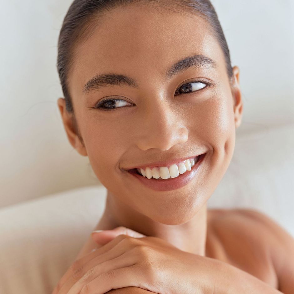 The woman is smiling and touching her face with her hand.