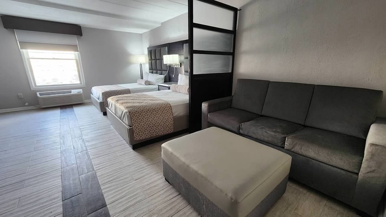 A hotel room with two beds , a couch , and an ottoman.