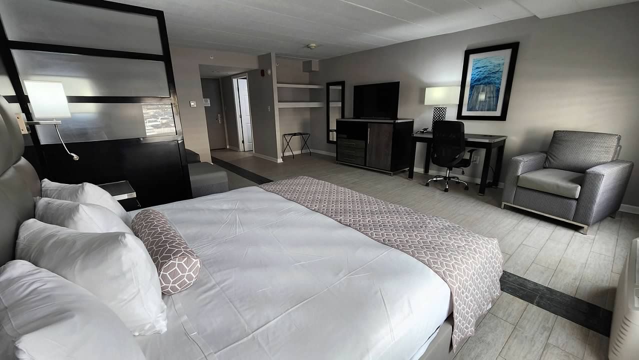 A hotel room with a king size bed , chair , desk and television.