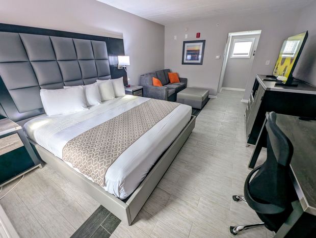 A hotel room with a king size bed , chair , desk and television.