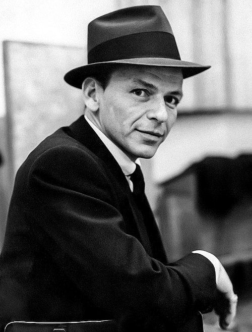 A man in a suit and hat is standing with his arms crossed.