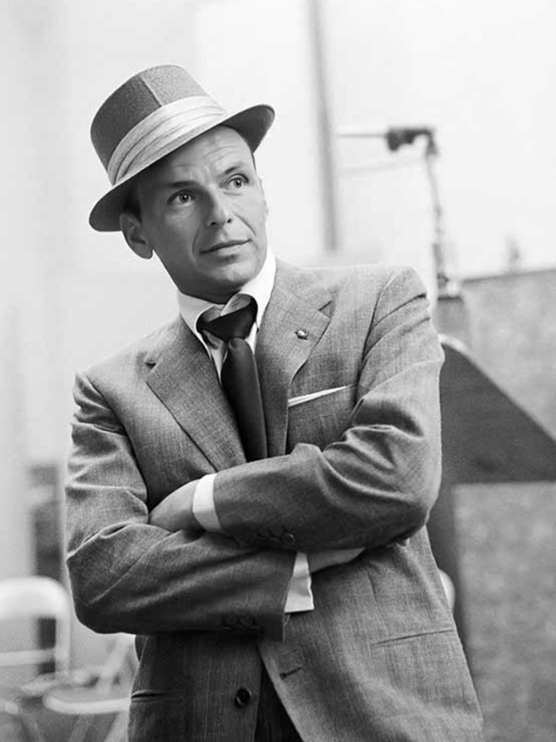 A man in a suit and hat is standing with his arms crossed.