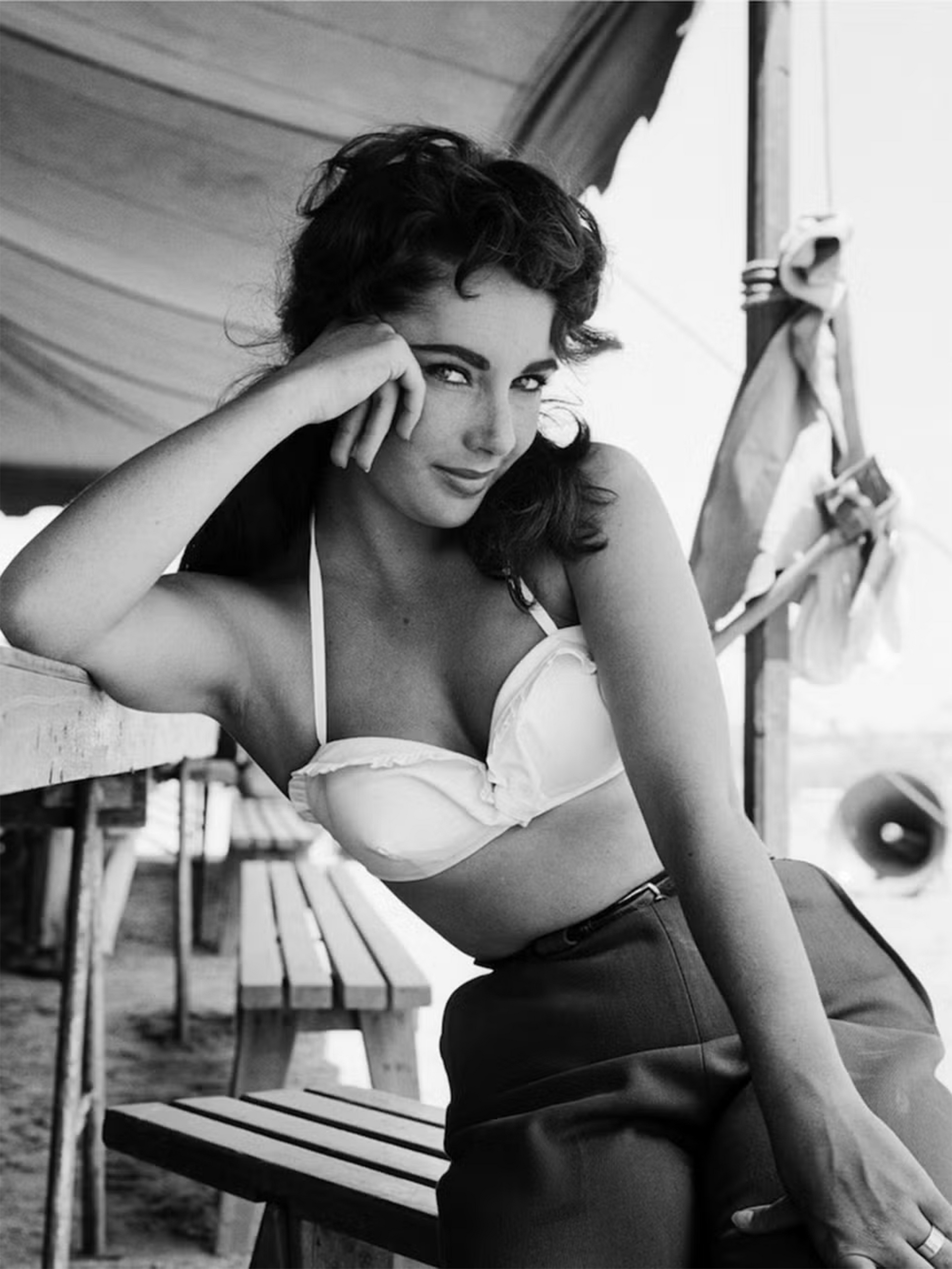 A black and white photo of a woman in a bikini sitting on a bench