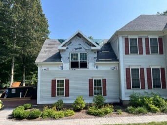 A white house with red shutters is under construction.