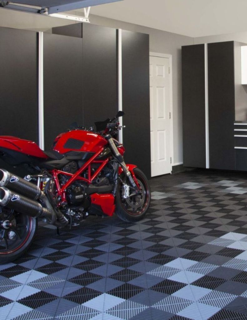 A red Ducati motorcycle parked in a modern garage with black storage cabinets and a gray-and-black checkered floor.