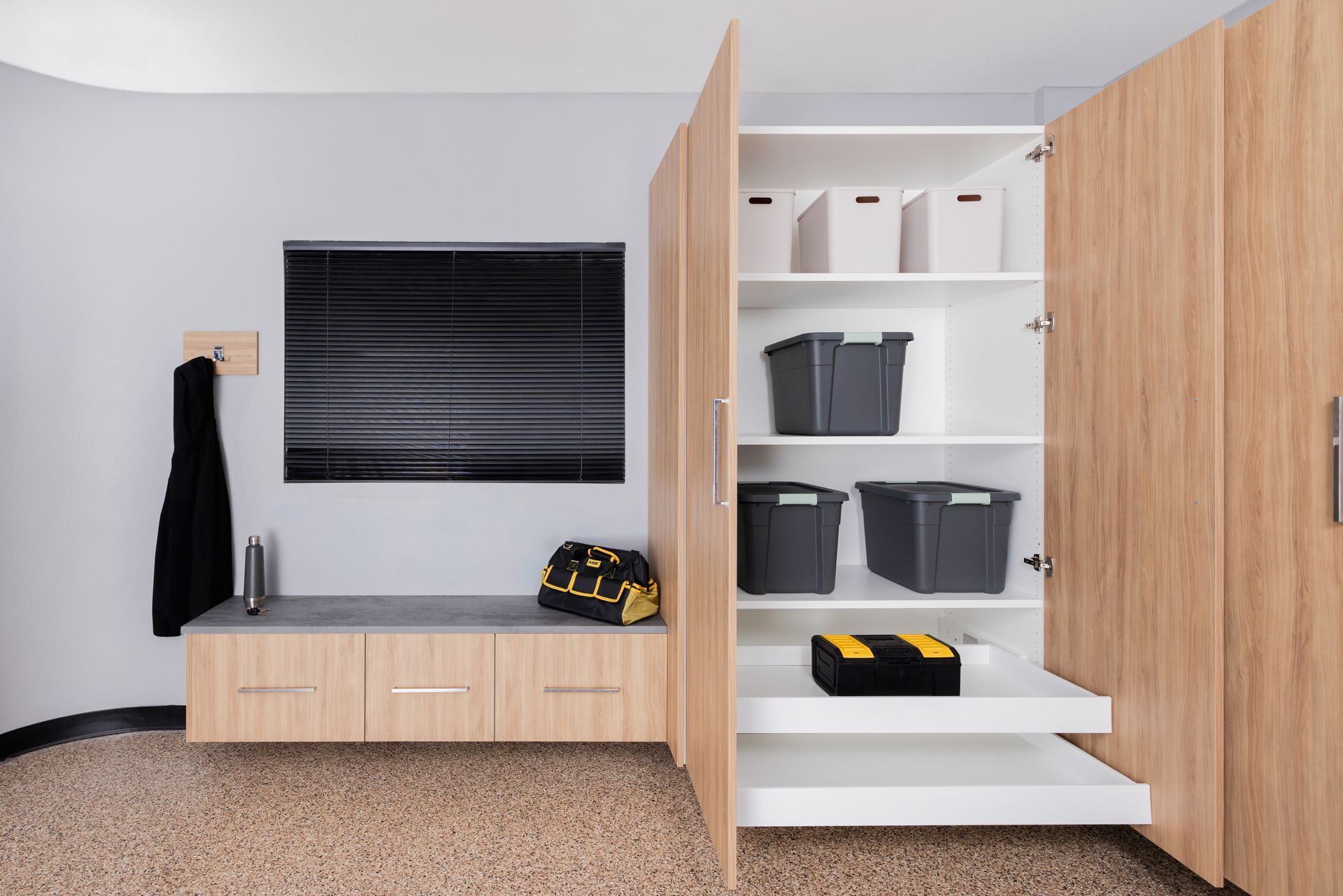 A modern entryway with a light wood bench, wall-mounted storage, a black television, and an open cabinet with organizers.