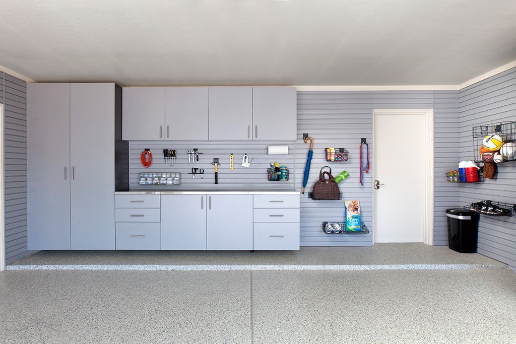 Light gray garage cabinets and storage organizers mounted on gray slatted walls with a concrete floor.