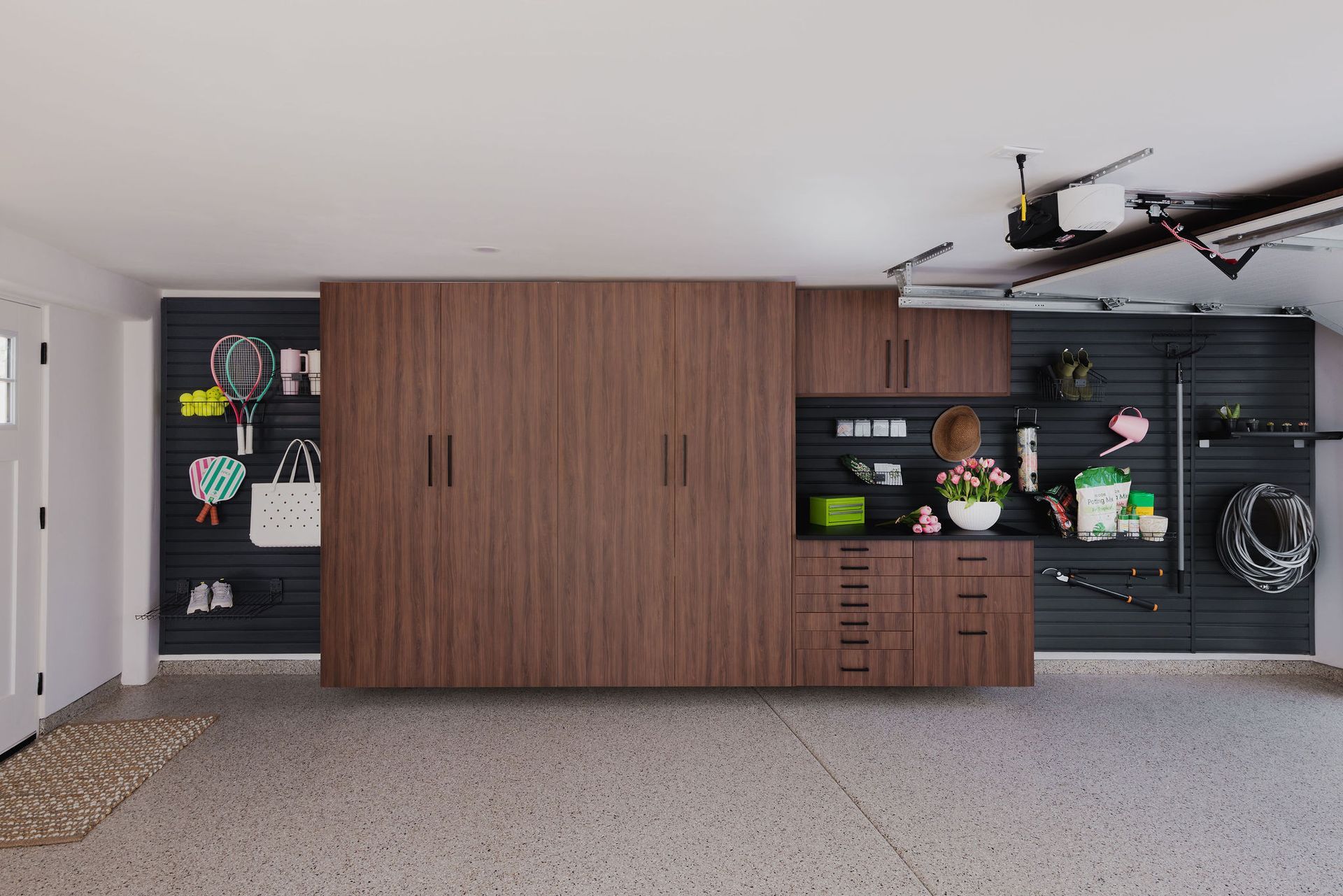 A sleek garage storage system with wood-toned cabinets and black slat walls for hanging tools and accessories.