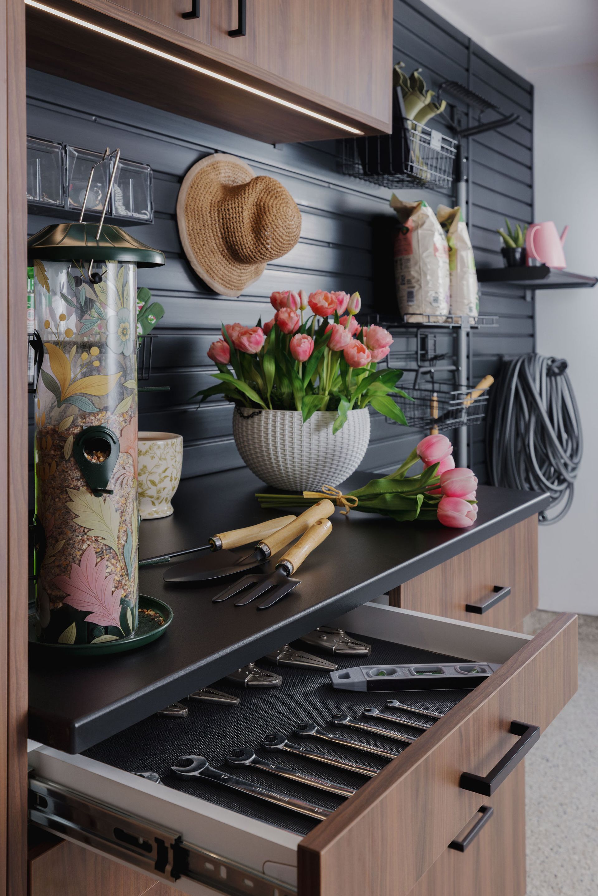 A workspace with a dark countertop featuring a bird feeder, flowers, and garden tools, with an open drawer of cutlery.