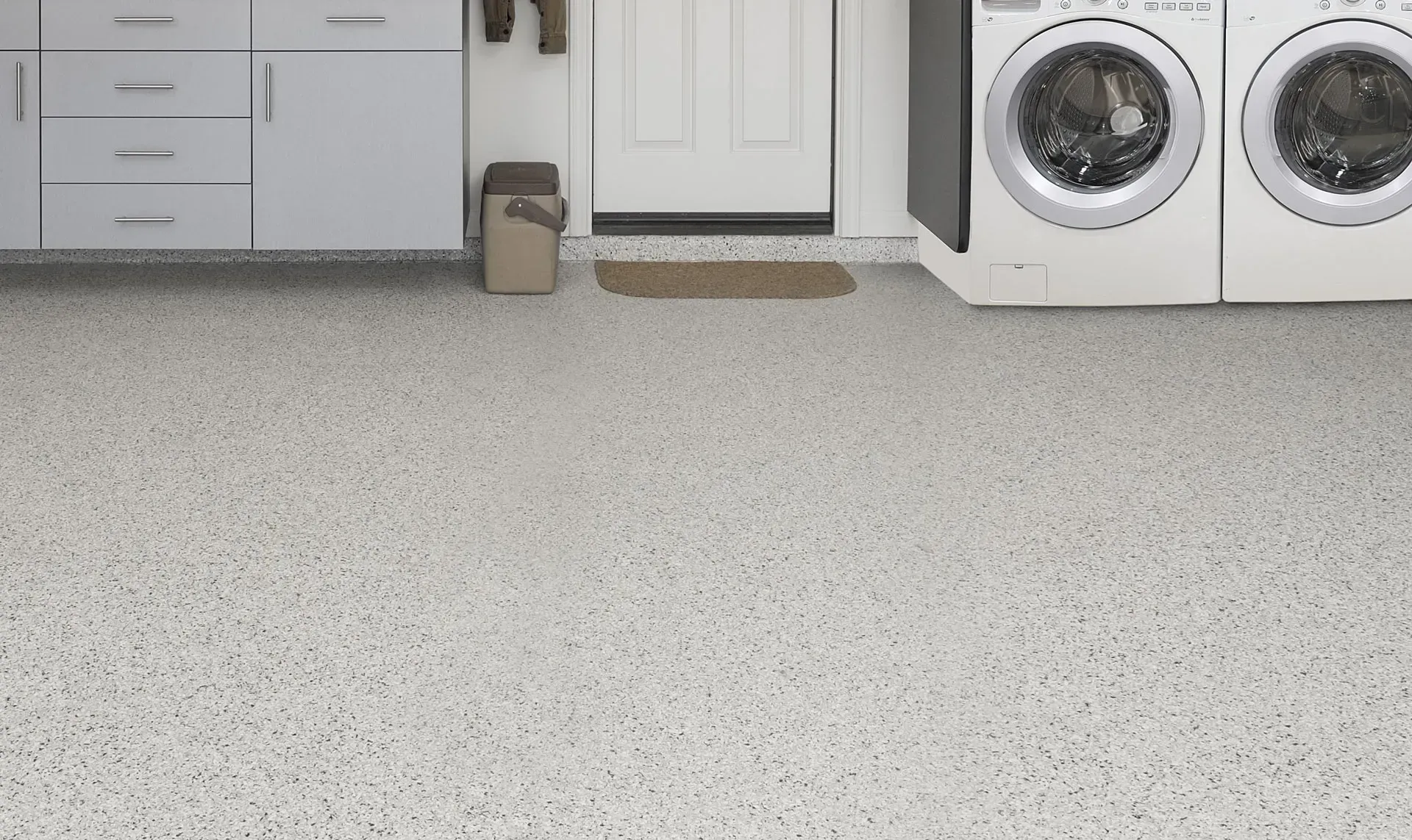 A laundry room with light gray cabinets, white appliances, and a gray speckled floor coating.