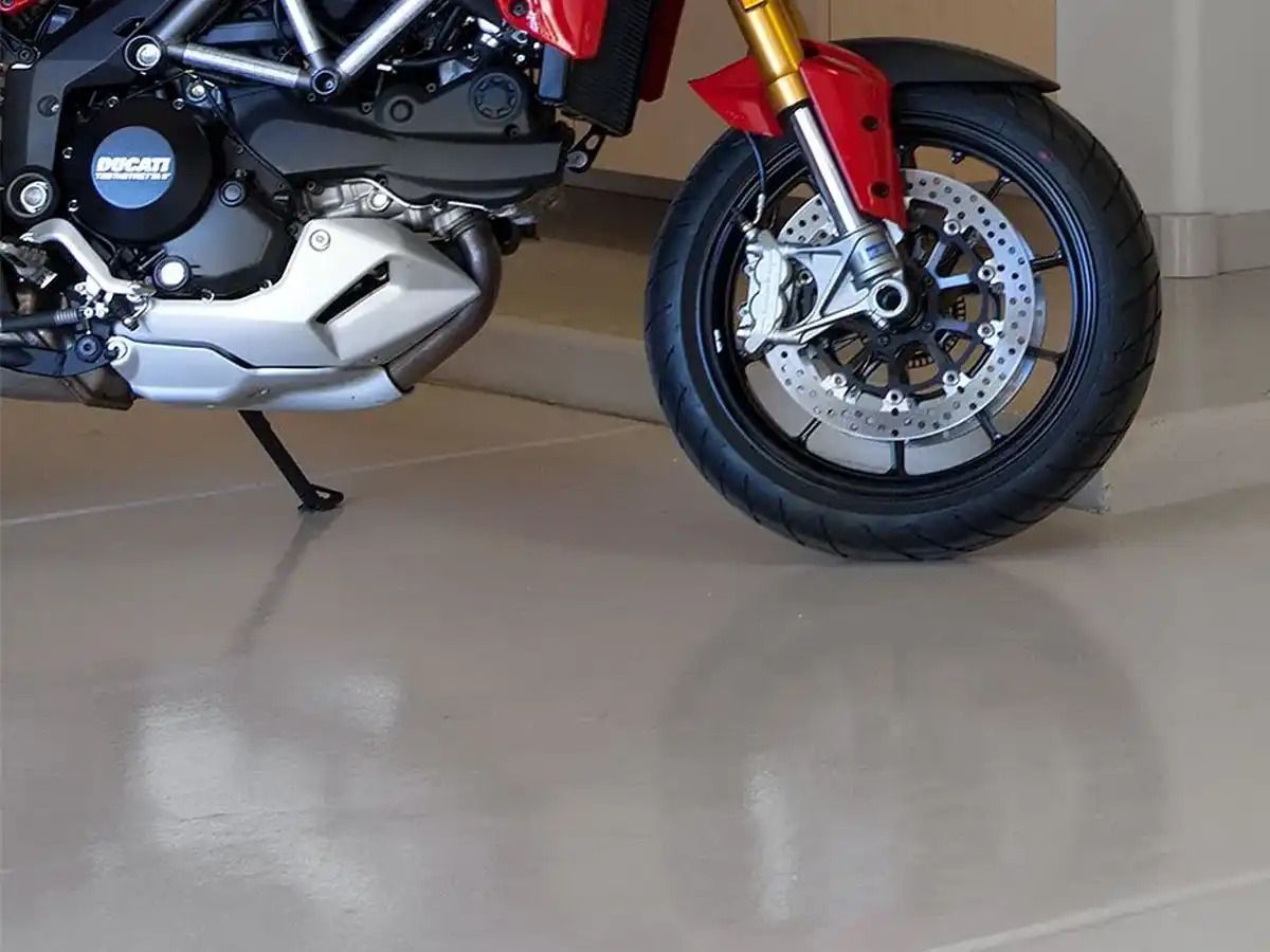 Close-up view of the front section of a red motorcycle parked on a smooth, reflective grey epoxy garage floor.