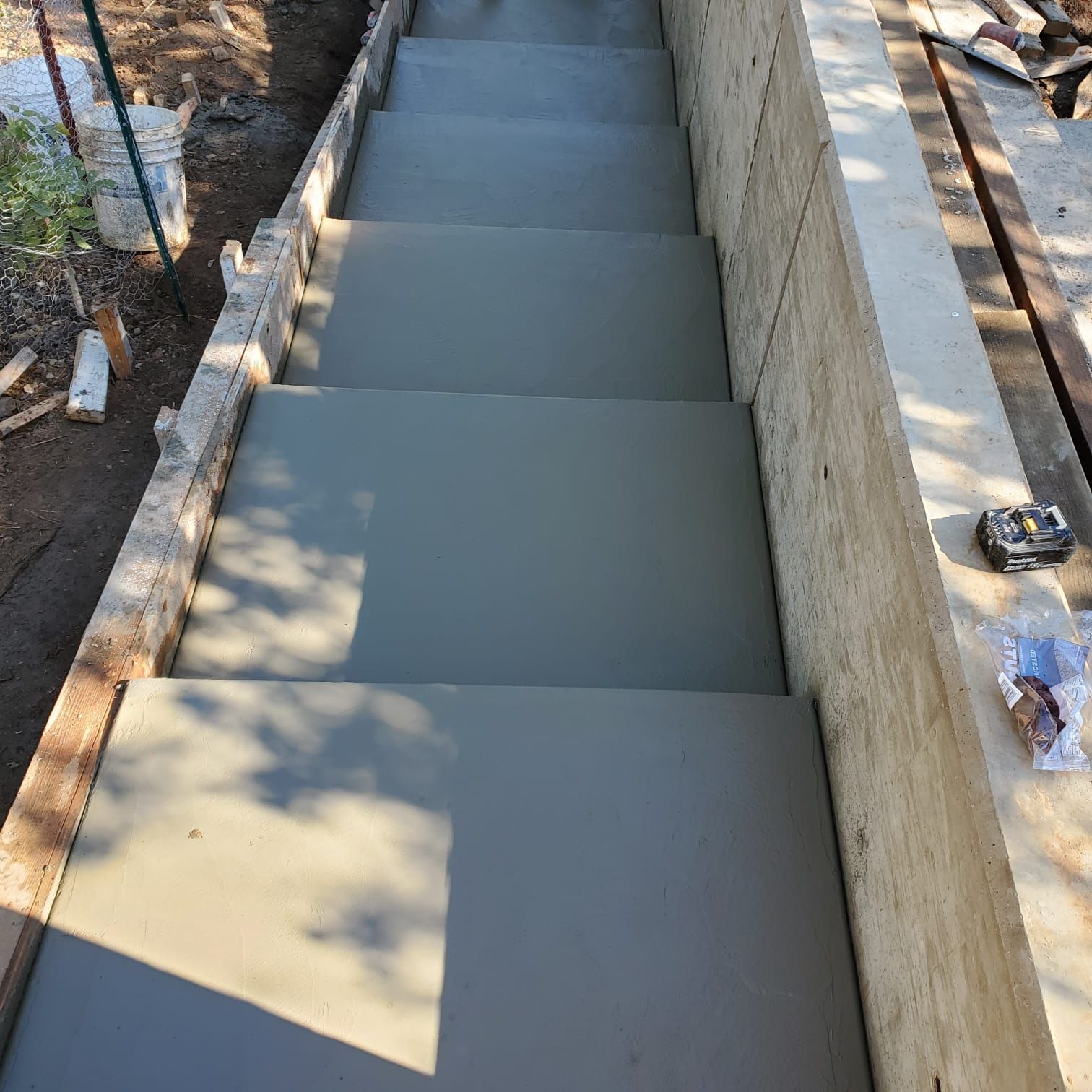 A top-down view of freshly poured concrete steps under construction, framed by wooden boards and a concrete retaining wall.