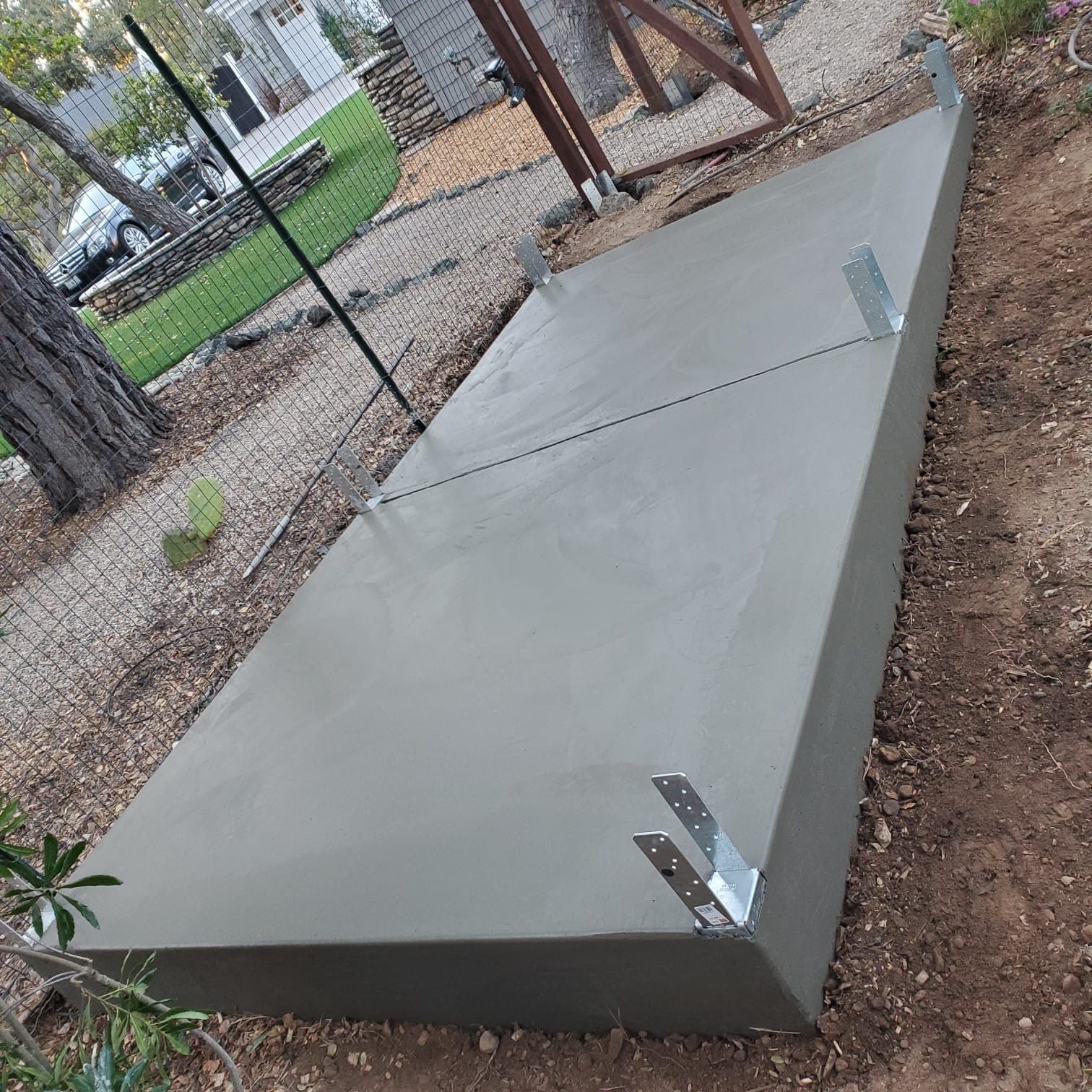 A newly poured rectangular concrete slab outdoors with metal post anchors embedded in the surface.