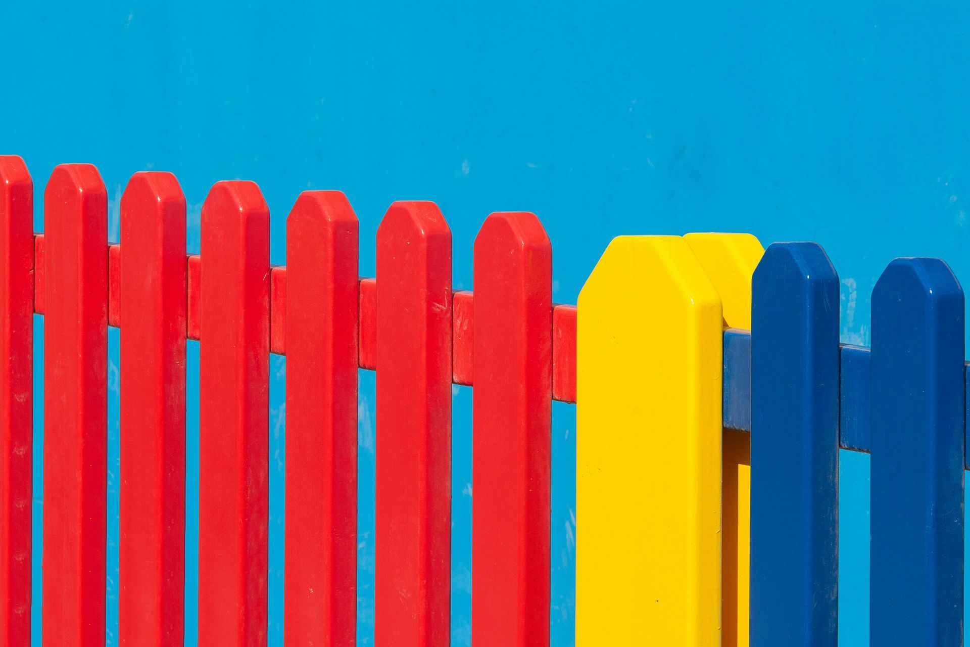 Red, yellow, and blue picket fence against a bright blue background.