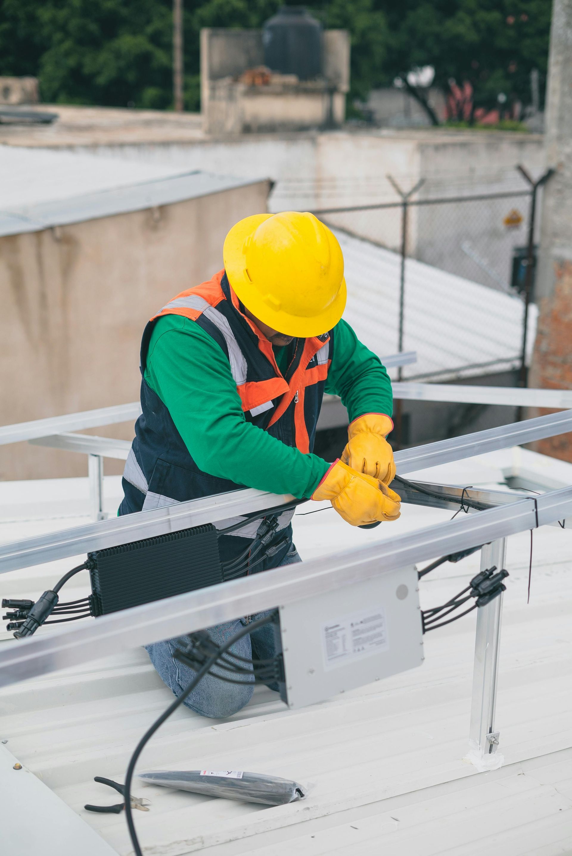 Worker in safety vest and hard hat installing solar panel on a rooftop.