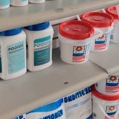 A shelf filled with bottles and buckets of pool chemicals.