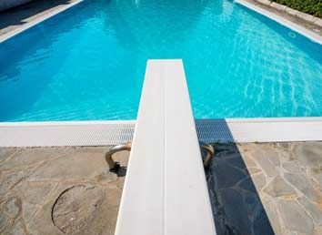 A diving board is sitting next to a swimming pool.