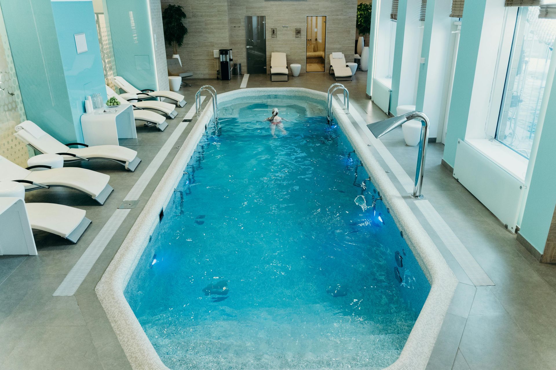 A woman is swimming in a large indoor swimming pool.
