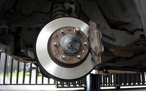 Car brake disc and caliper, under a vehicle, showing wear and tear.
