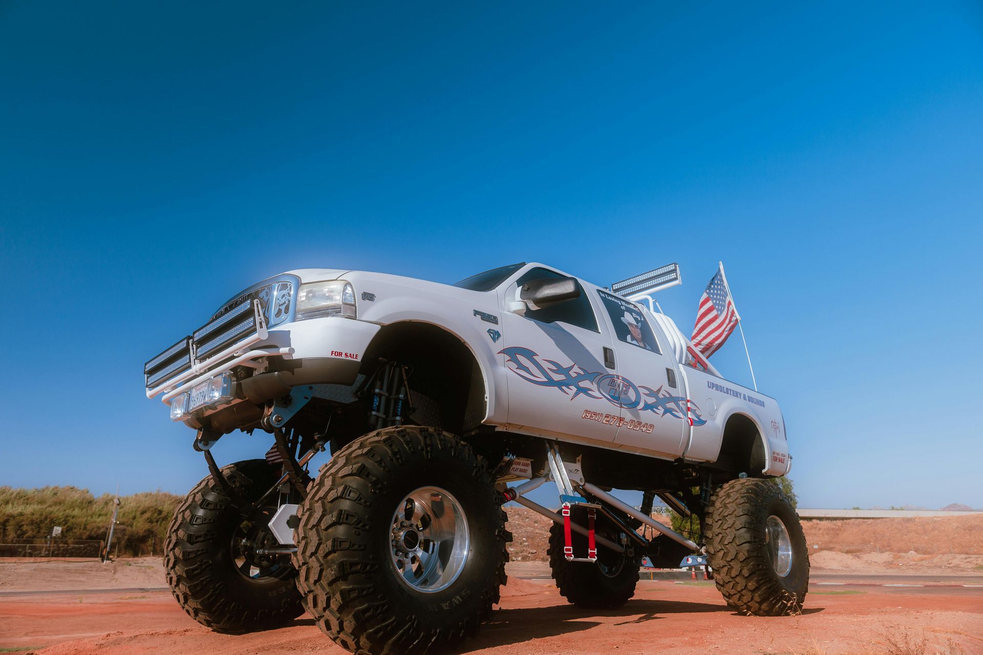 White monster truck with American flag against a blue sky.