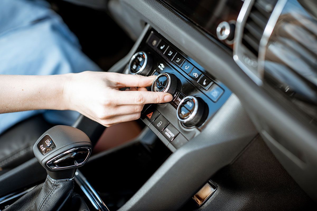 Hand adjusting car climate control knob in a car interior.