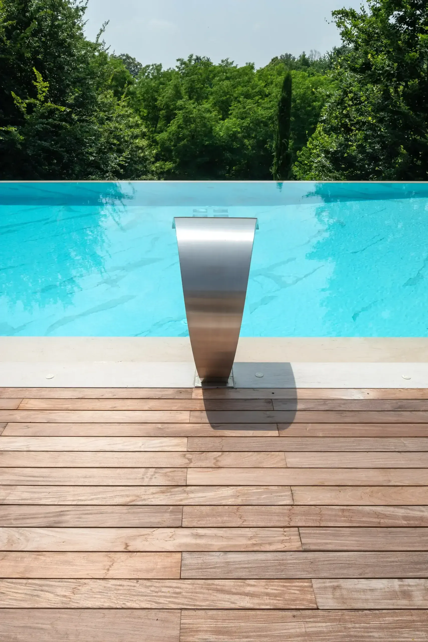 Una piscina con una terrazza in legno e alberi sullo sfondo.
