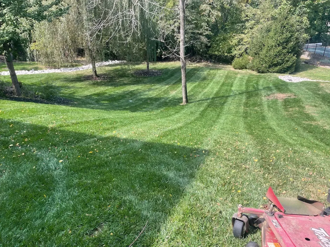 Lawn being mowed with a riding mower, creating striped patterns in the green grass on a sunny day.