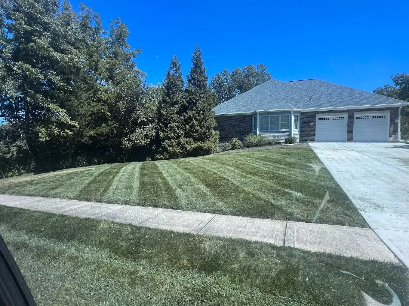 Lawn with freshly mowed stripes in front of a house with a driveway and garage doors on a sunny day.