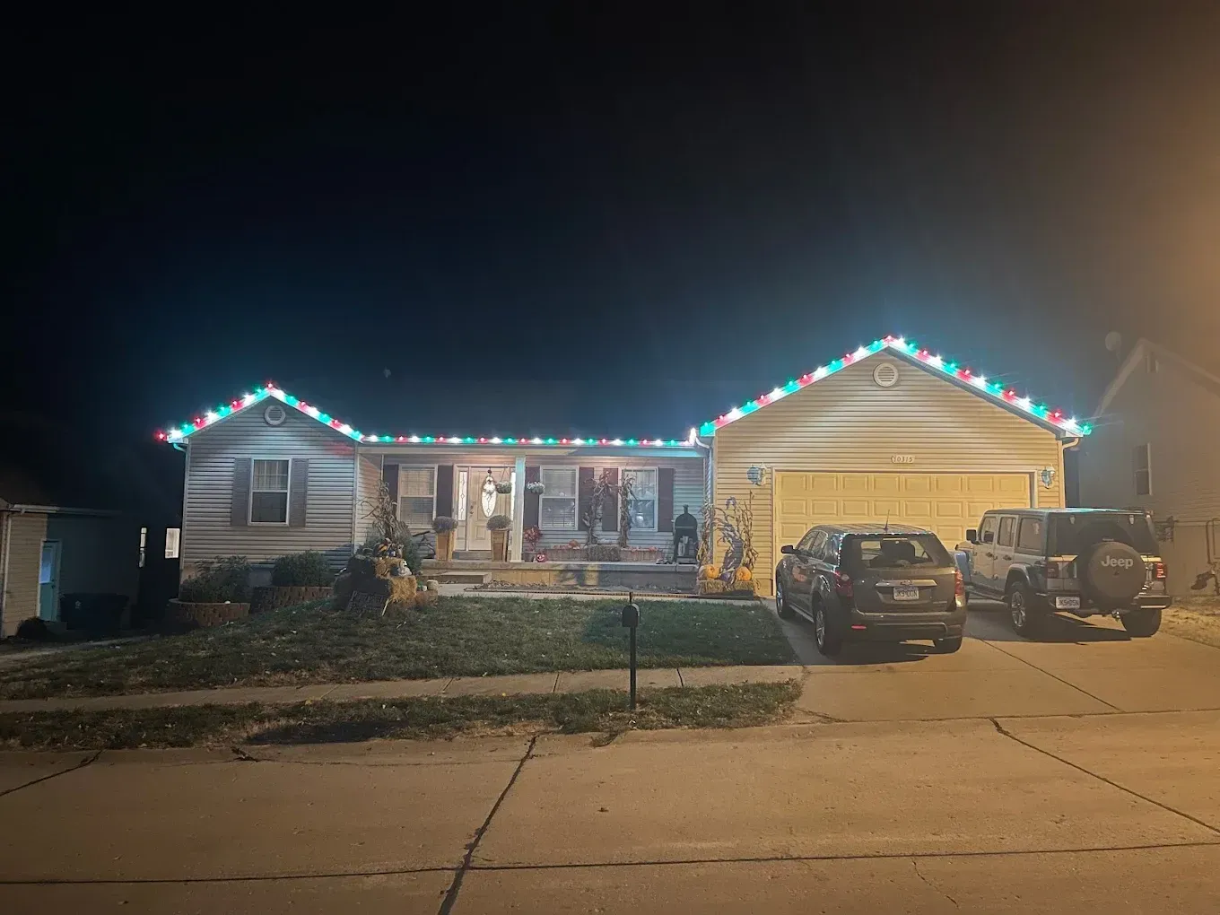 House decorated with Christmas lights at night; cars parked in the driveway.