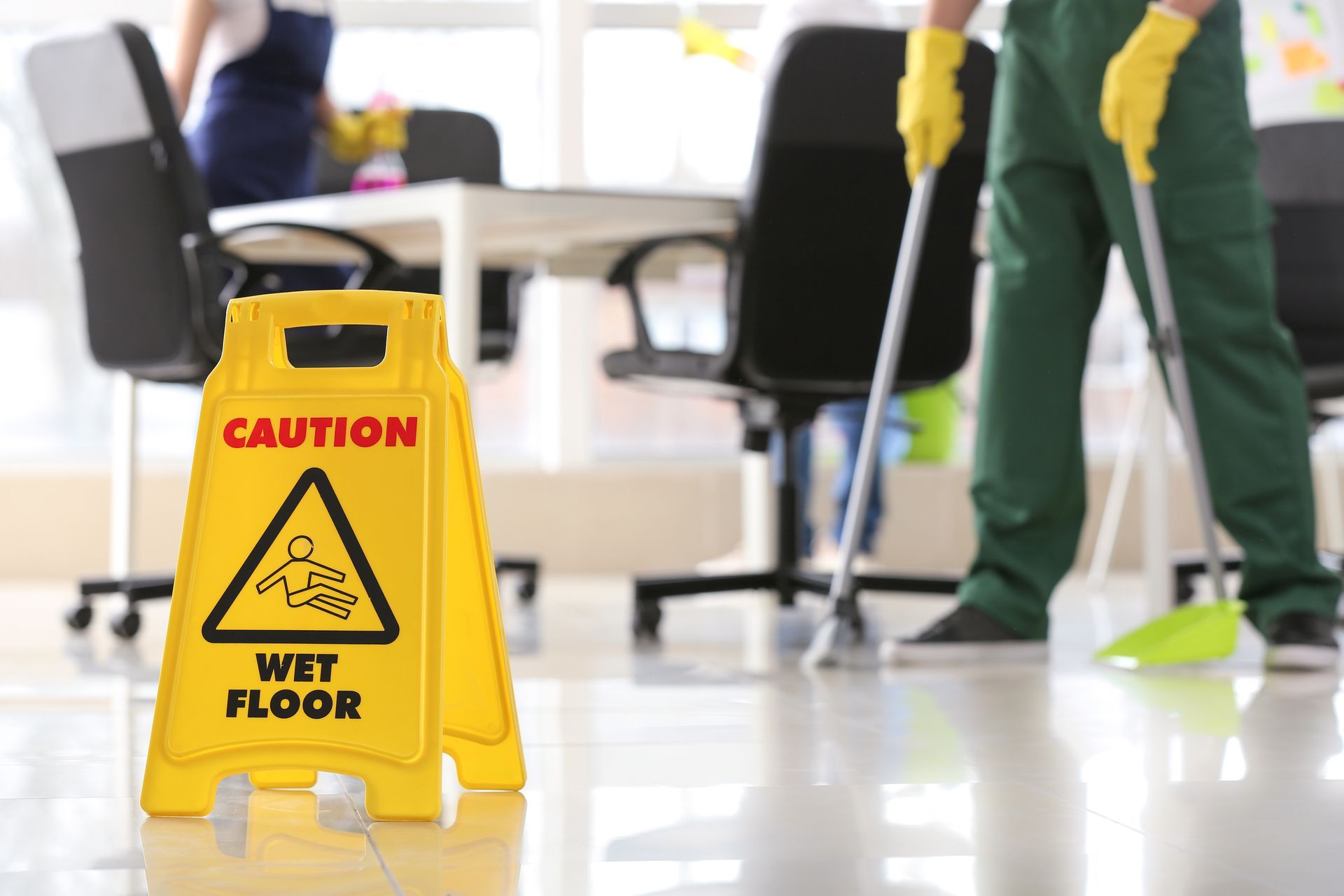 Yellow wet floor caution sign in an office with people mopping the floor
