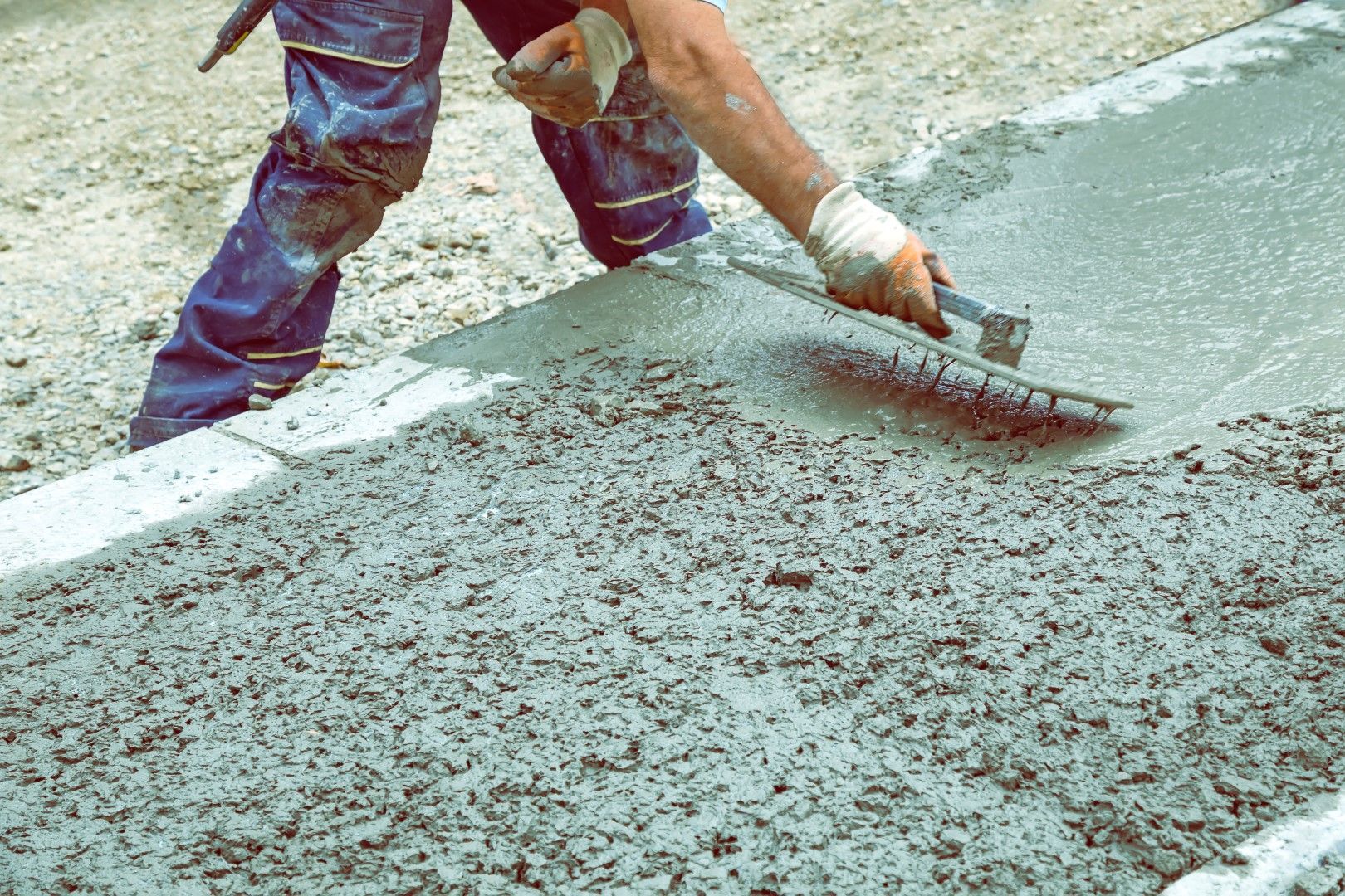 A man is spreading concrete on the ground with a trowel.
