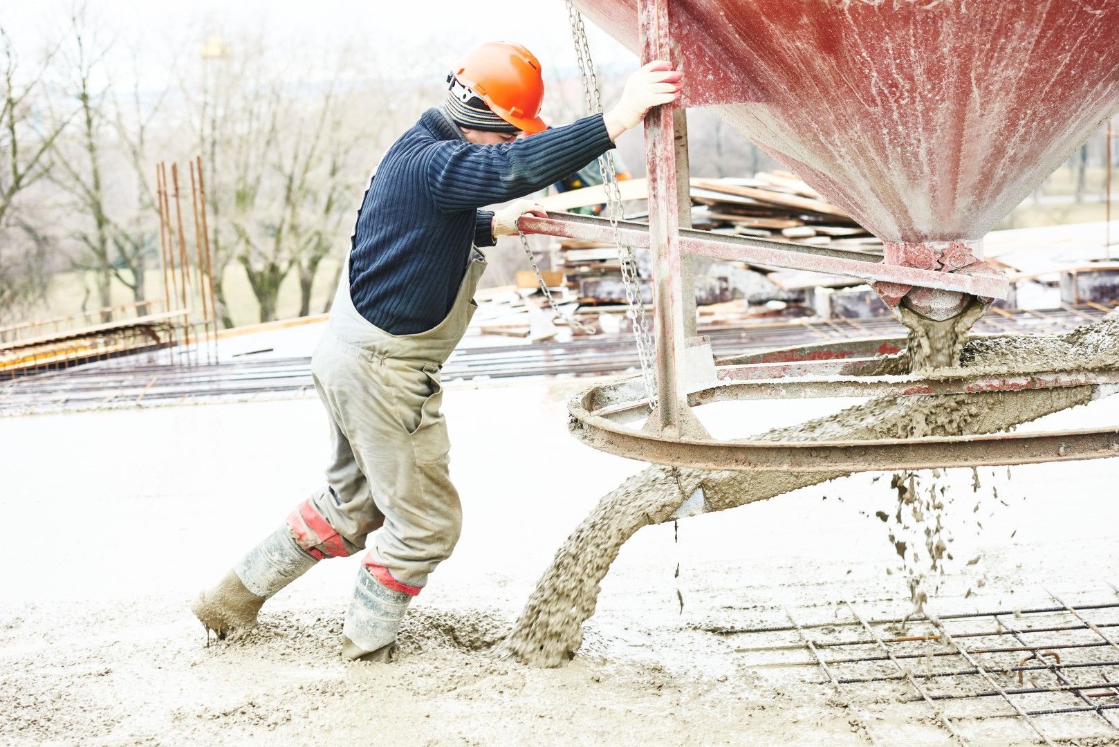 A construction worker is pouring concrete into a concrete mixer.