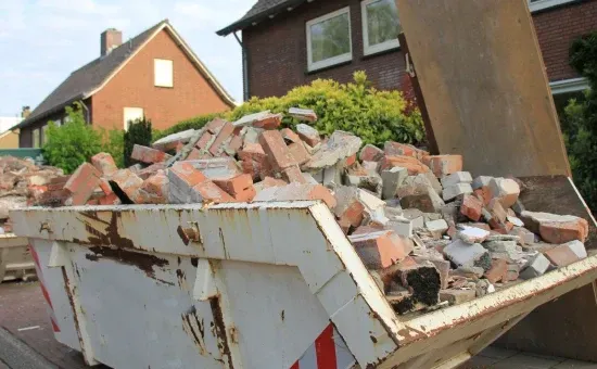 A dumpster filled with bricks is sitting in front of a house.