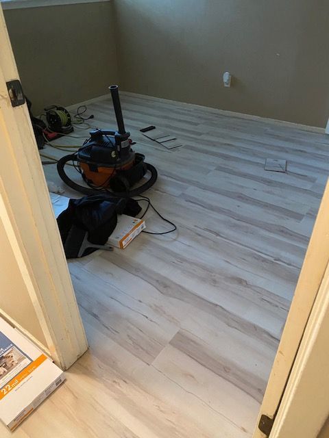 Light wood-look flooring in a room, a vacuum cleaner sits in the center. The room is light brown, seen through a doorway.