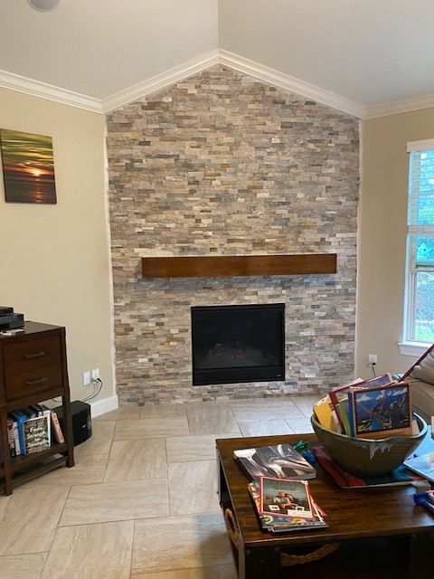 Fireplace with stone accent wall and wooden beam mantle. Beige tiled floor, dark wooden coffee table.