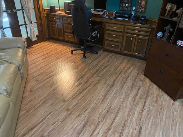 Wooden-look flooring in a home office with a desk, cabinets, chair, and bookcase. Beige couch on the left.