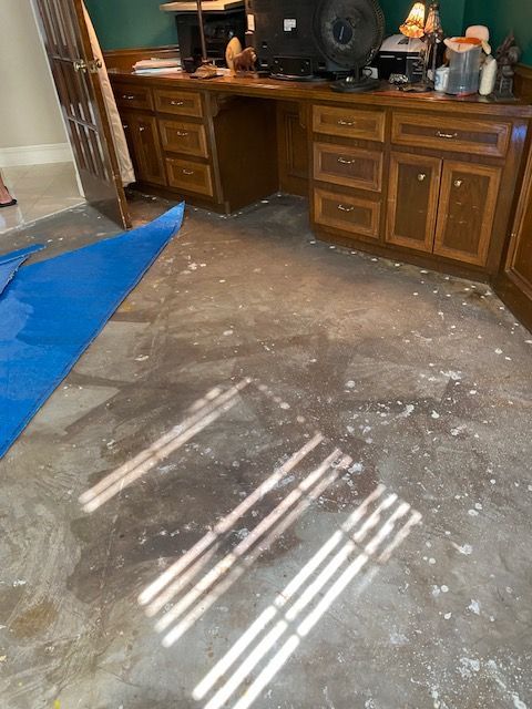 Room with dark wood cabinets, a desk, and a wet, speckled concrete floor. Sunlight streams across it.