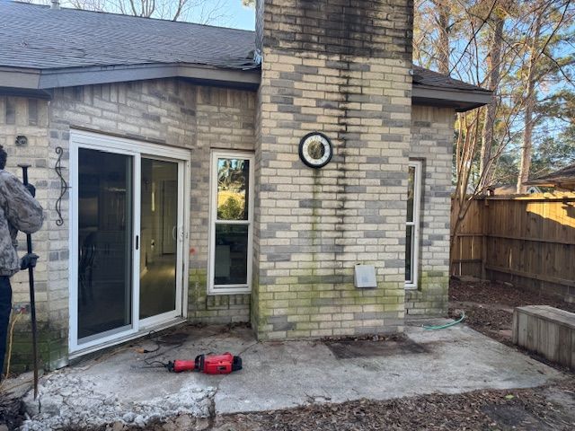Backyard view of brick house with concrete patio, chimney, sliding door, and windows.