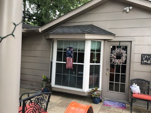 Exterior of a house with a bay window, a door with a wreath, and an American flag hanging in the window.