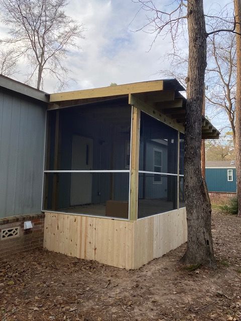 Screened porch addition on a house, featuring wooden framing, screen panels, and a low wooden wall.