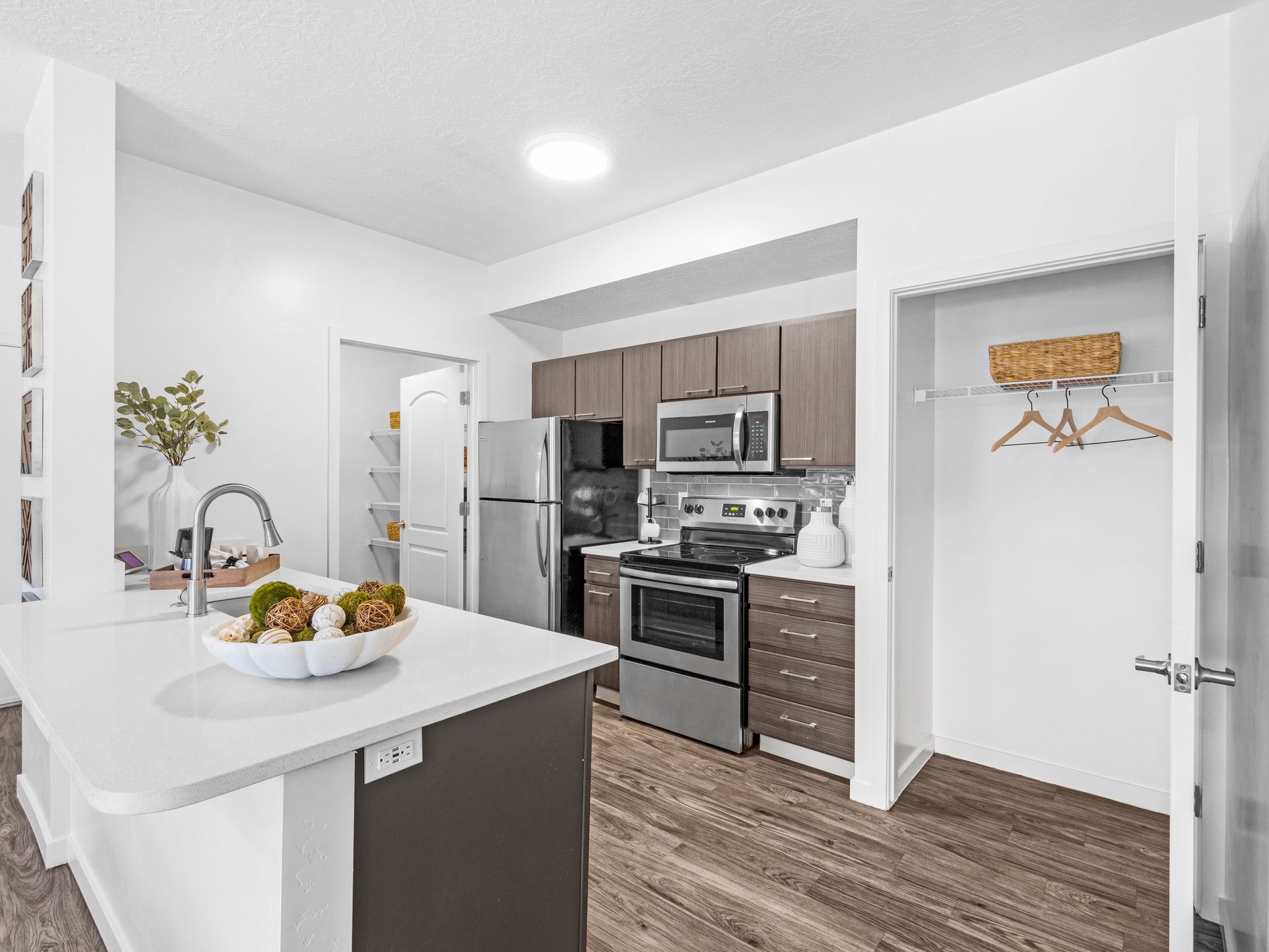 Modern apartment kitchen with stainless steel appliances, island, and a closet with hangers.