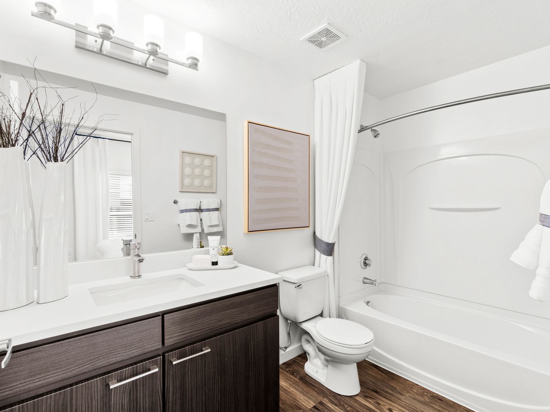 Modern bathroom with white sink, dark wood vanity, large mirror, toilet, and tub/shower.