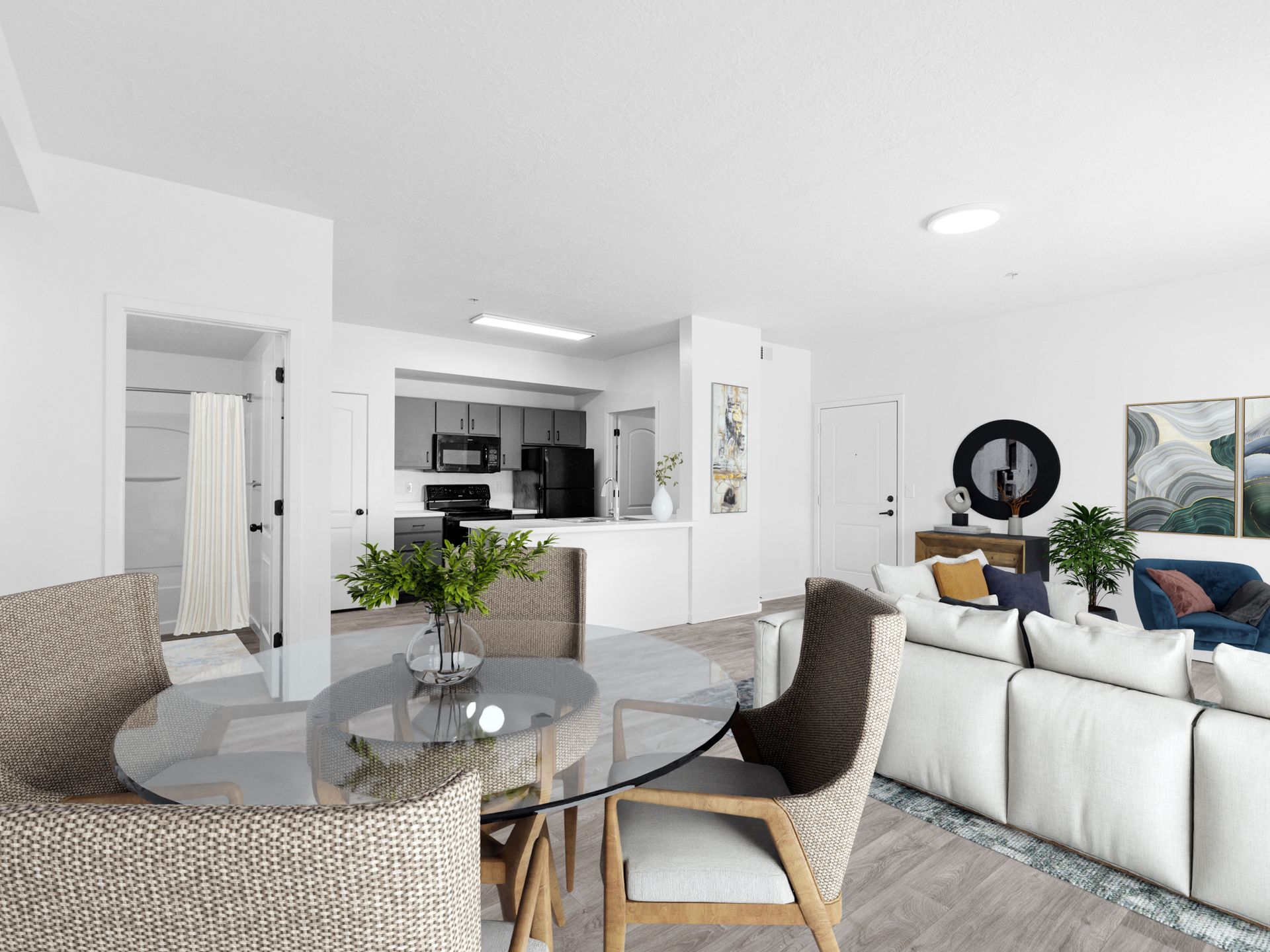 Bright open-plan living area with glass round dining table, beige chairs, white kitchen, and sofa.