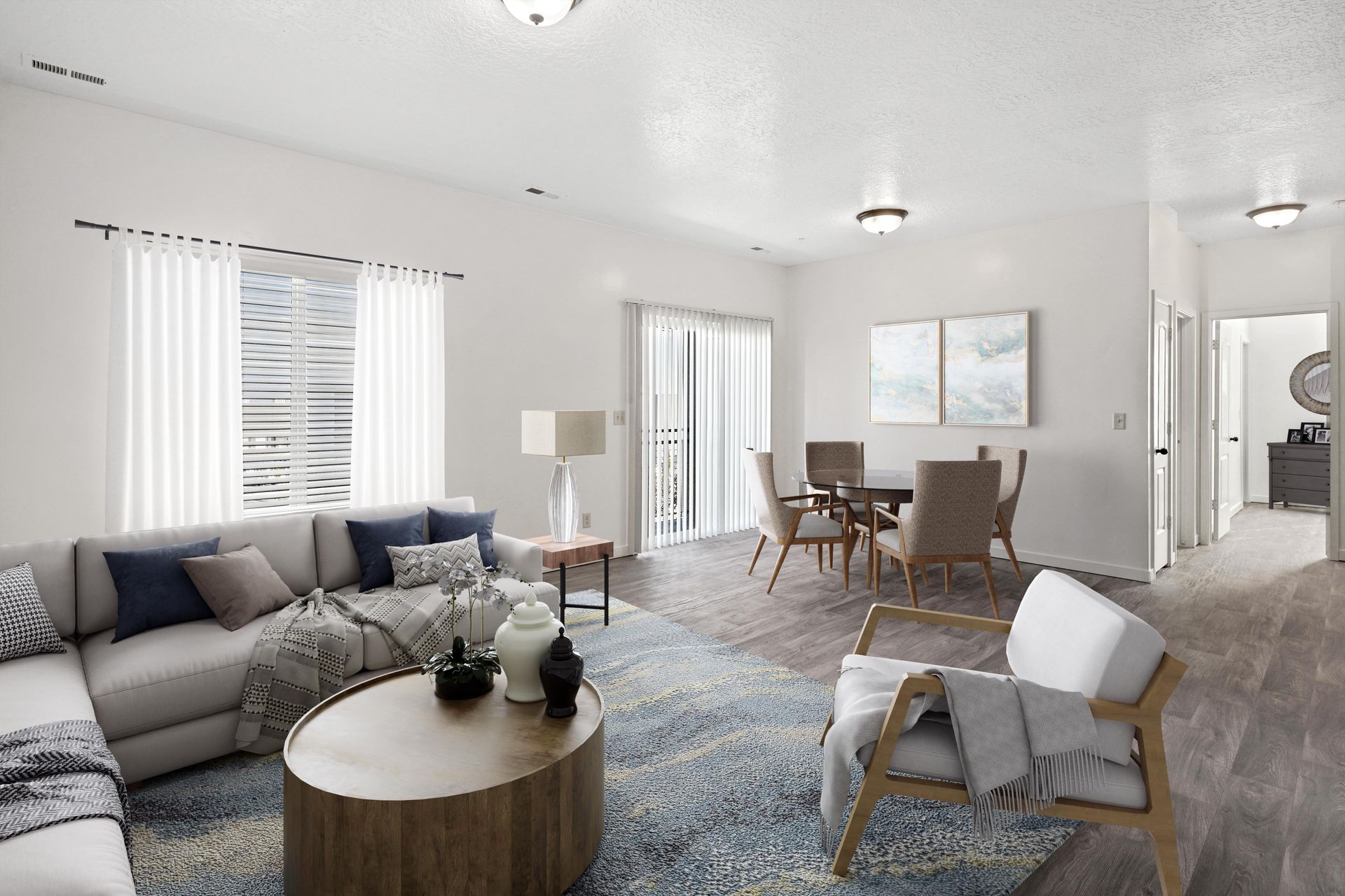Bright apartment living room with beige sectional sofa, round wooden coffee table, and a dining area.