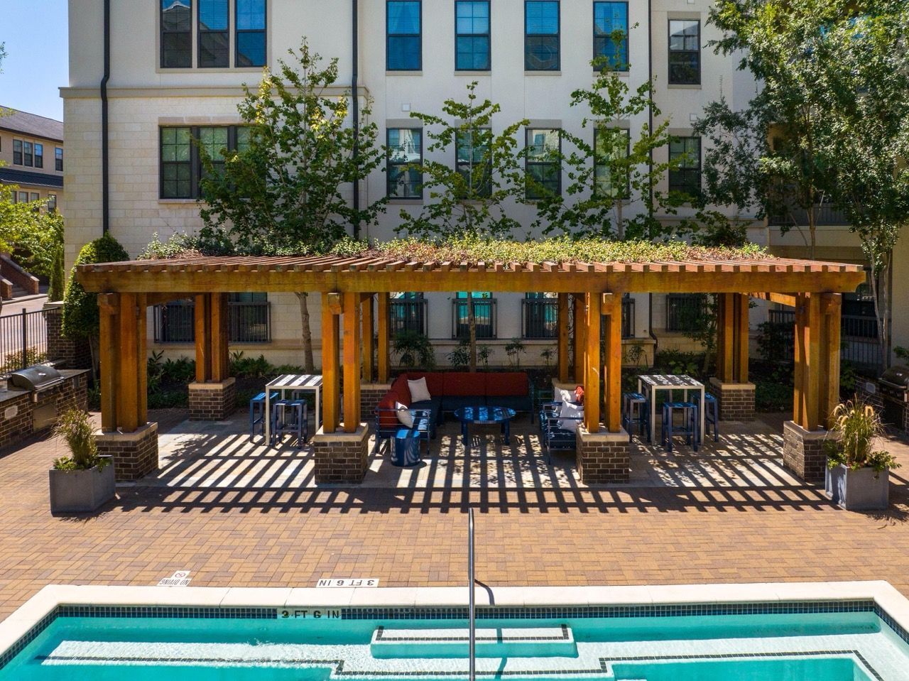 Outdoor pool area with wooden pergola, lounge seating, and planters in a residential courtyard.