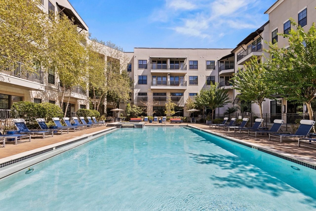 Outdoor pool area of an apartment complex with lounge chairs and surrounding buildings.