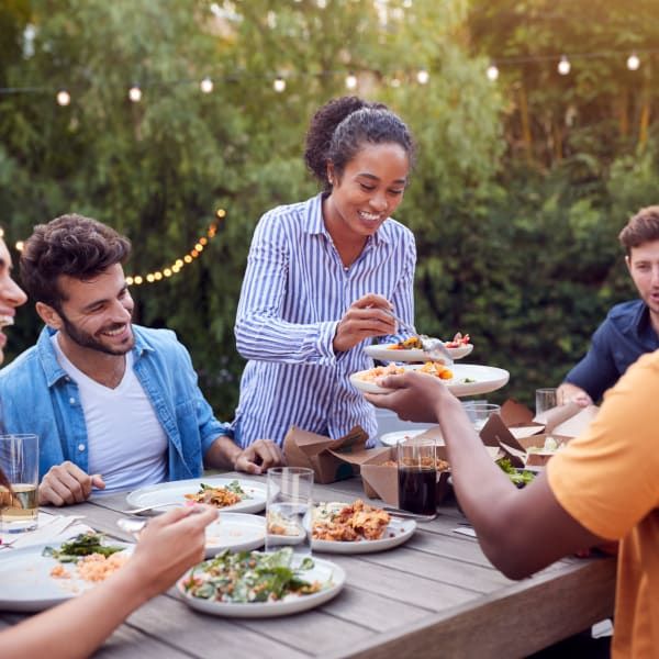 A group of people eating dinner together at an outdoor table with string lights in the background.