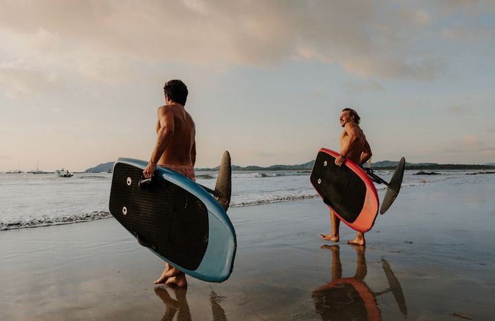 two men are walking on the beach holding surfboards .