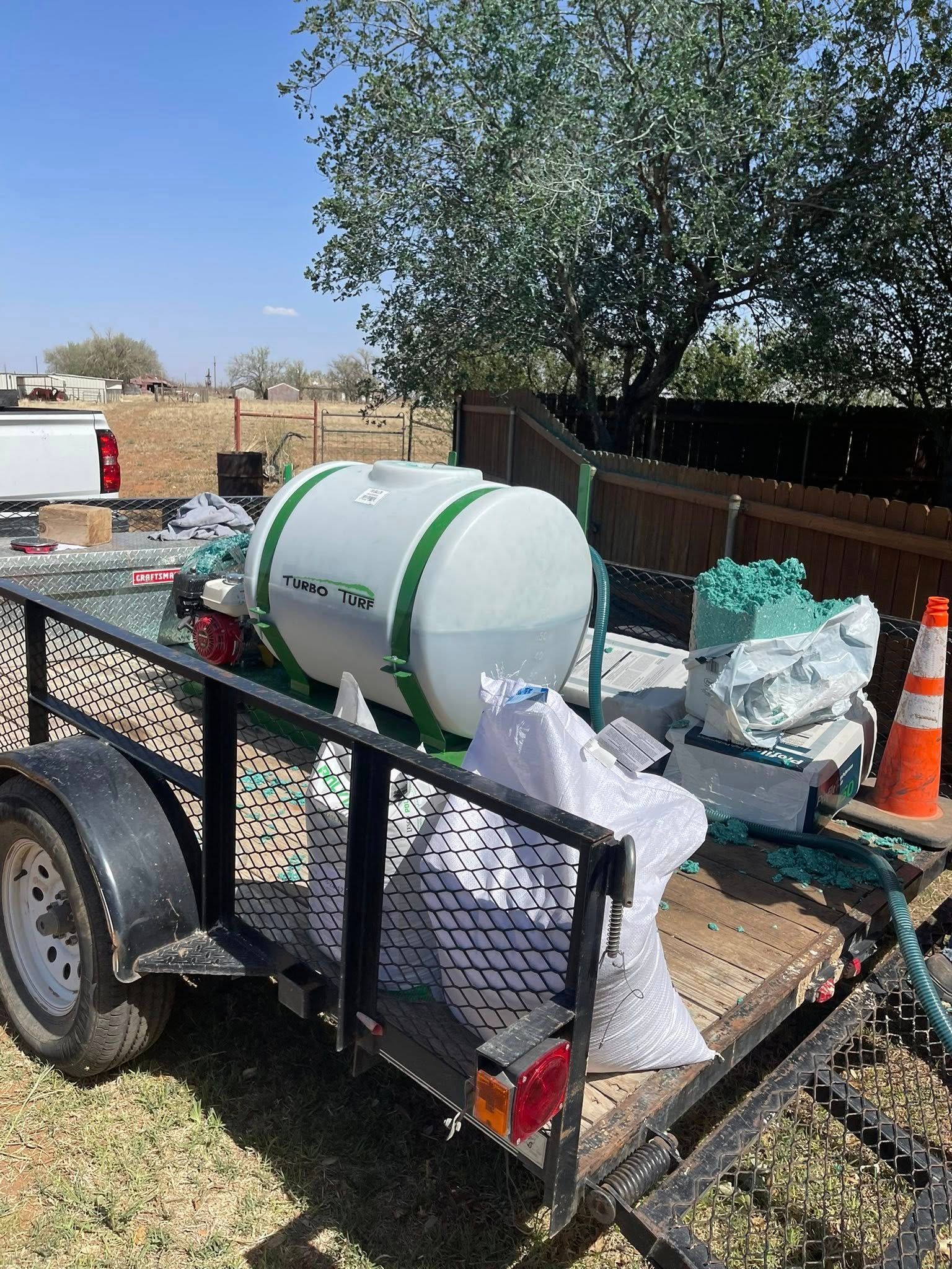 Trailer with a large white tank, green trim, and various supplies outdoors under a blue sky.