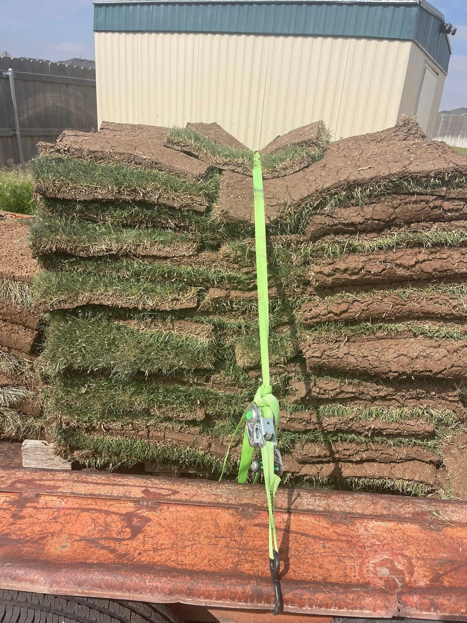 Stacks of sod secured with a green strap on a rusty flatbed trailer.